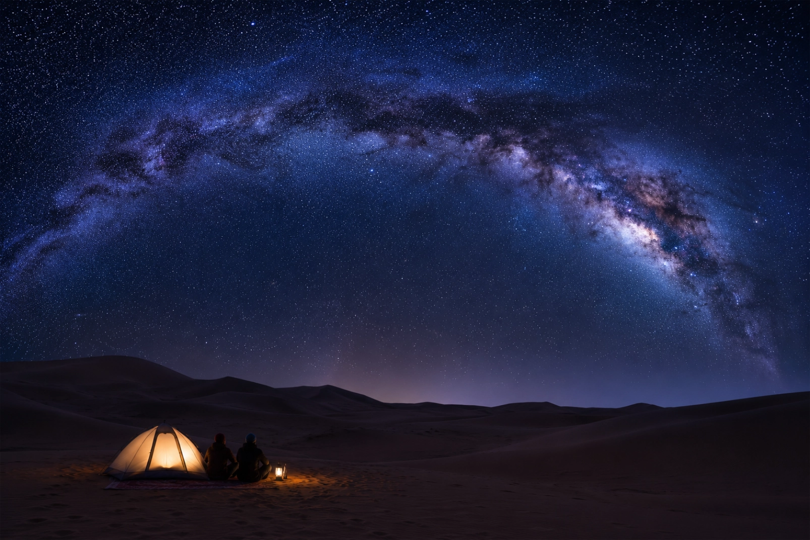 A breathtaking night sky over the Sahara desert, the Milky Way arching brilliantly across a star-filled sky, silhouetted sand dunes below, a tiny lit tent or two stargazers in the foreground for scale, deep blue and violet tones, ultra-clear dark skies far from city light.